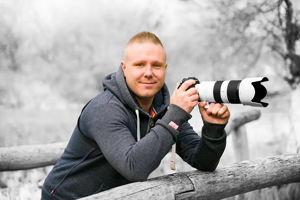 Billede af fotograf der står på en træbro med et 70-200mm objektiv siddende foran på sit kamera